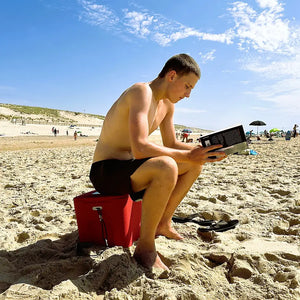 Box in Größe M rot am Strand mit jungem Mann darauf sitzend